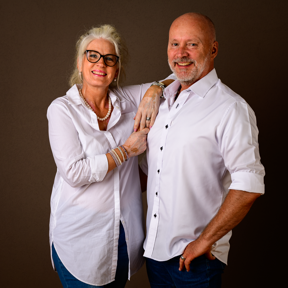 Unsere Verbindung ist besonders - Jeder ist einzigartig. Nicole und Felix stehen nebeneinander in einem Raum mit warmer Beleuchtung. Sie lächeln in die Kamera und vermitteln ein herzliches Willkommen bei MindArt@KIWI.
